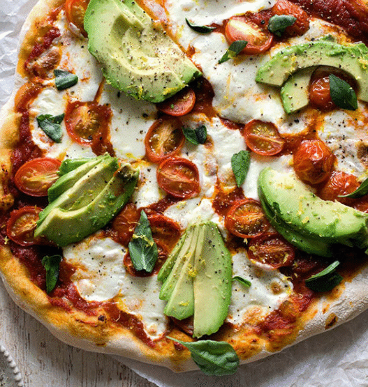 Avocado & Heirloom Tomato Pizza topped with arugula and basil on golden crust