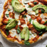 Avocado & Heirloom Tomato Pizza topped with arugula and basil on golden crust