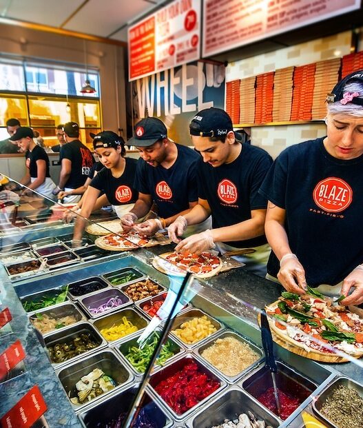 Freshly baked Blaze Pizza being pulled from a fast-fire’d oven with custom toppings