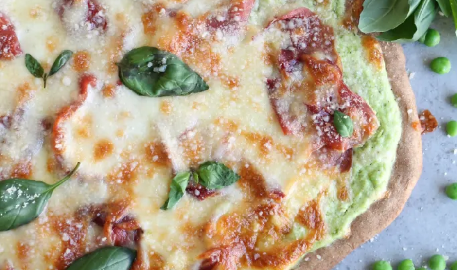 Freshly baked lemon ricotta and pea shoot pizza on a wooden board, garnished with lemon zest and pea shoots